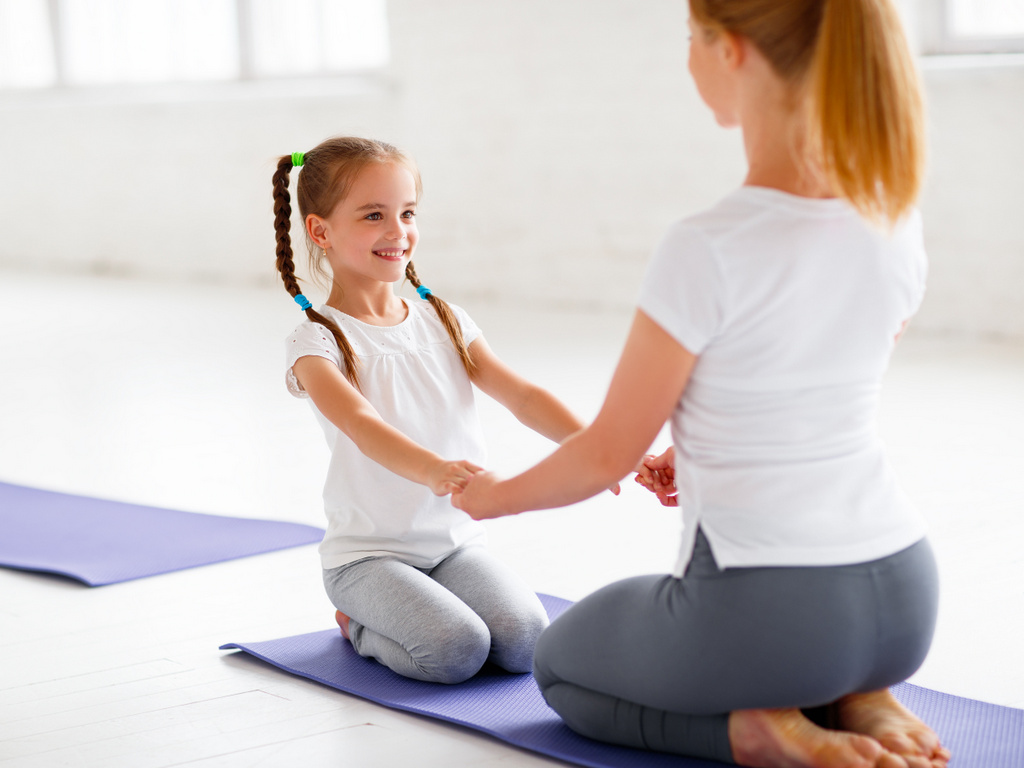 Une mère et sa fille se tiennent la main en position du diamant (yoga)